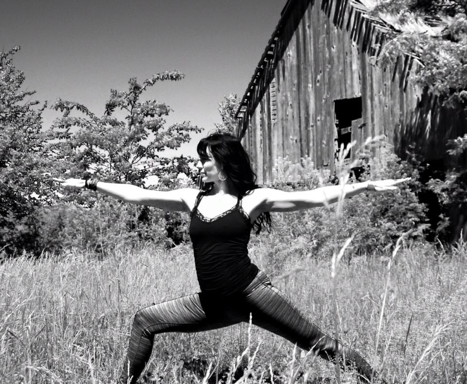 Black and white image of a white brunette woman doing Warrior Two yoga pose outside in the grass